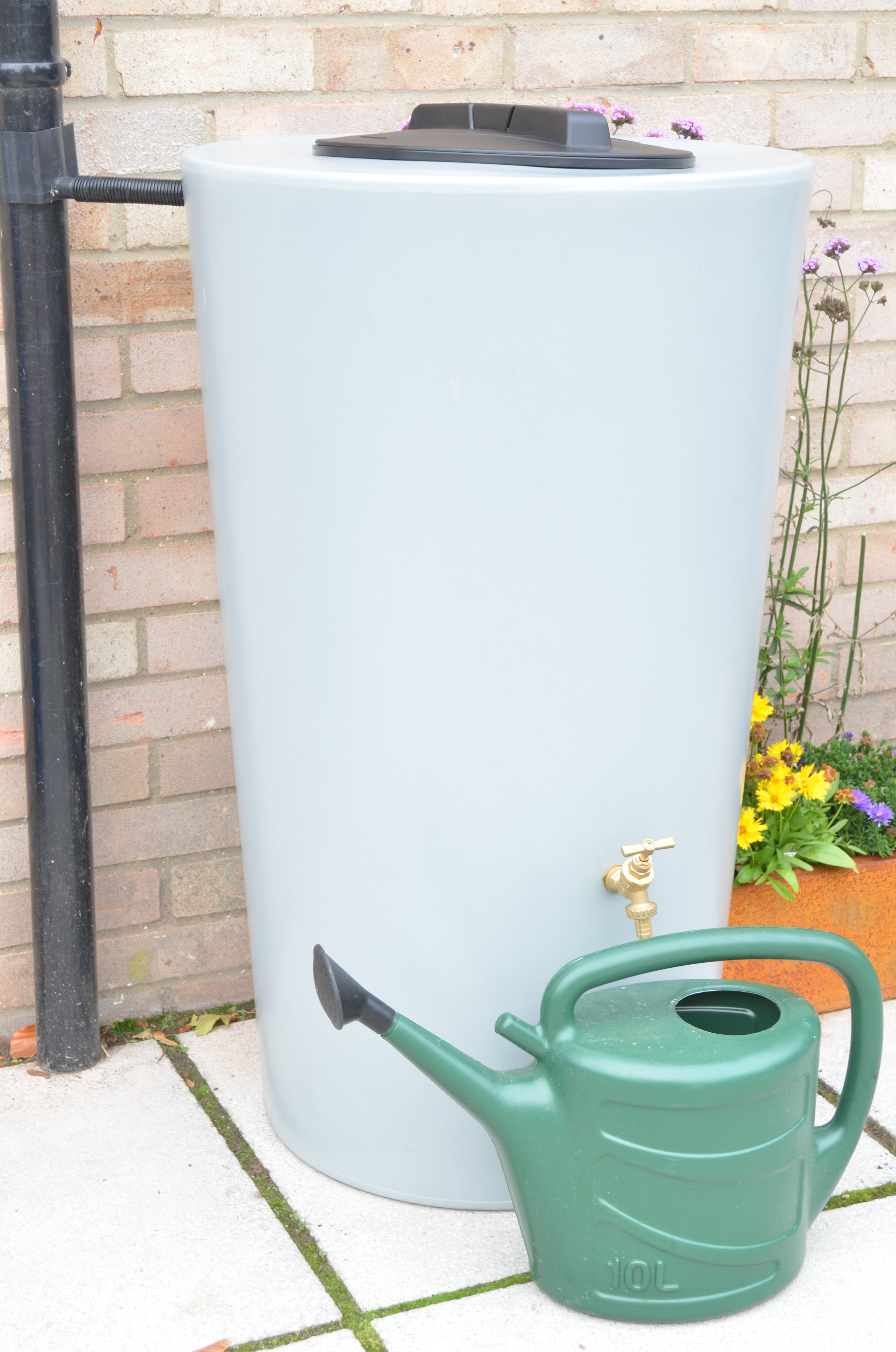 Green watering can with a grey water butt with plants in the background